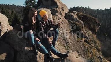 恋爱中的年轻夫妇坐在岩石上和朋友视频聊天。旅游、交流、休息、聊天理念